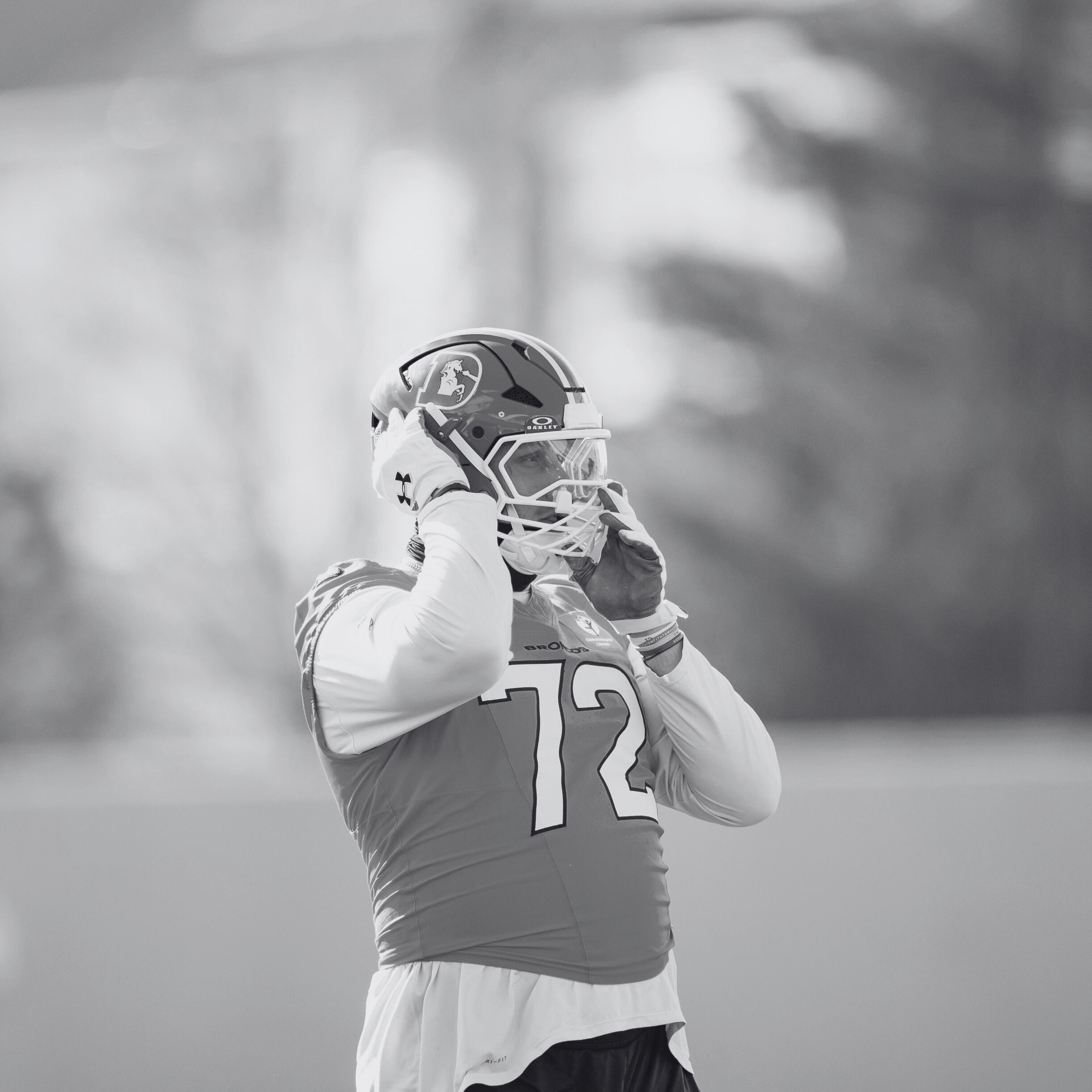 Black and white photo of a football player holding a helmet on a field